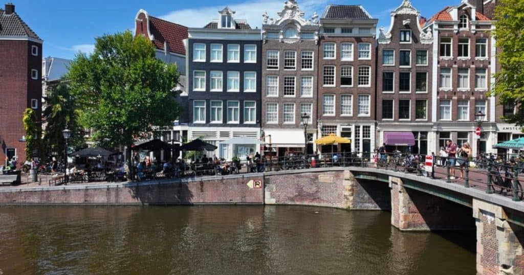Amsterdam canal houses and canalside terraces in summer, the view that answer part of why are Amsterdam hotels so expensive.