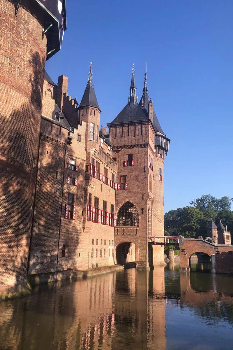 De Haar Castle's brick gatehouse tower with three spires, seen across the moat with reflections in the water.