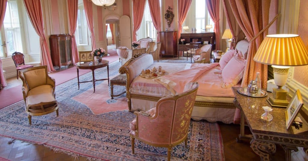 A pink and gold sitting room at De Haar Castle with silk drapes, antique chairs, and a canopied bed.