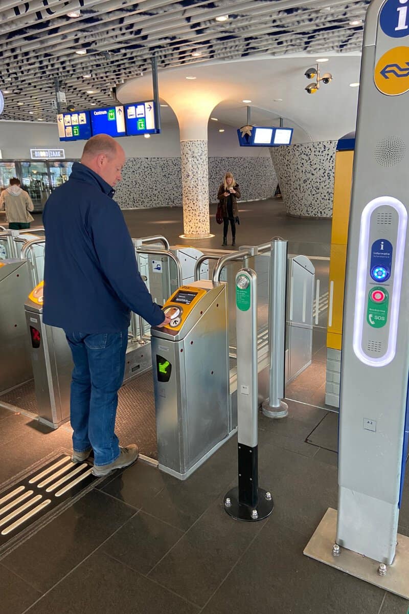 Gerrit tapping his card on the yellow check-in post at the gates of a Dutch railway station.