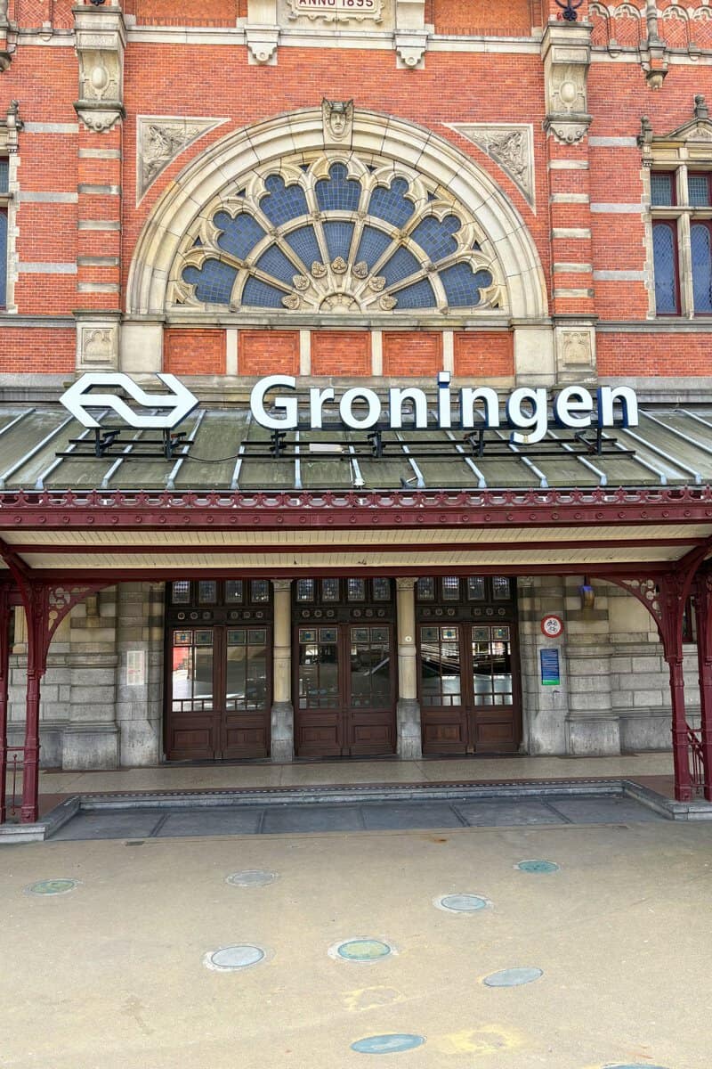 Historic red brick facade of Groningen railway station from 1895 with the NS logo above the entrance.