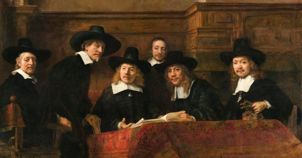 Group portrait by Rembrandt of the five sampling officials of the Amsterdam drapers' guild, in black clothing and wide-brimmed black hats, seated behind a table covered with a red Persian carpet with an open ledger in front of them, one man half-rising from his chair, a bareheaded servant standing behind, all looking up toward the viewer. One of the top paintings at the Hals-Rembrandt Exhibition.