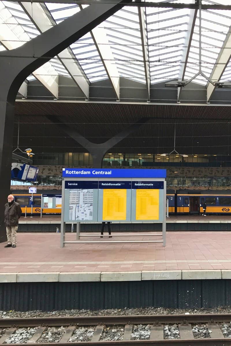 Rotterdam Centraal platform sign and timetable boards under the station's glass roof with an Intercity train waiting in the background.